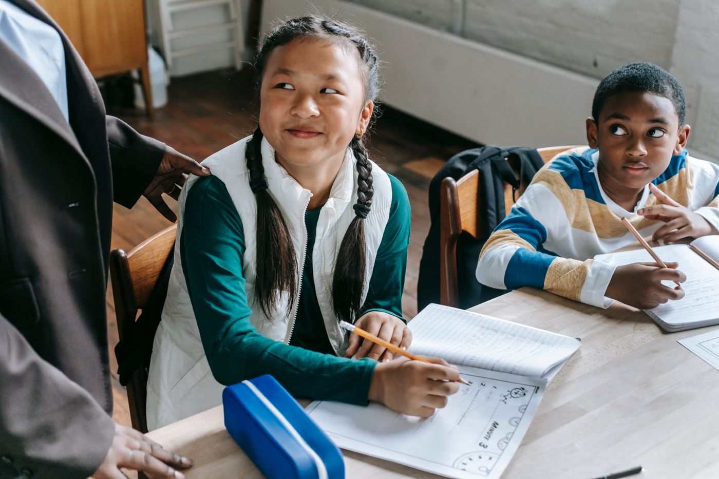 A teacher supporting two students with their schoolwork at a classroom desk